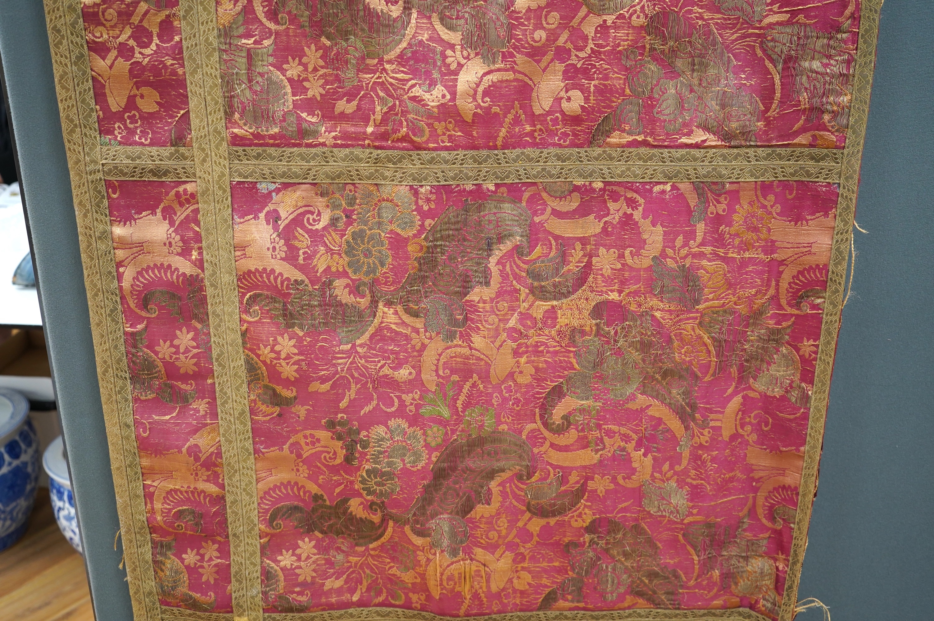 A fine 17th century Italian crimson silk brocade wall hanging, originally woven with gold threads and polychrome silks in a large ornate floral pattern, possibly part of a larger hanging, the front now edged with later n